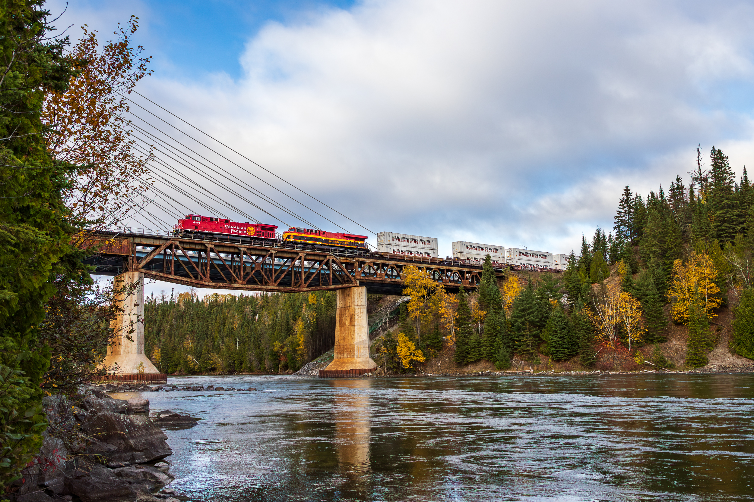 Train crossing a bridge over a river surrounded by autumn trees