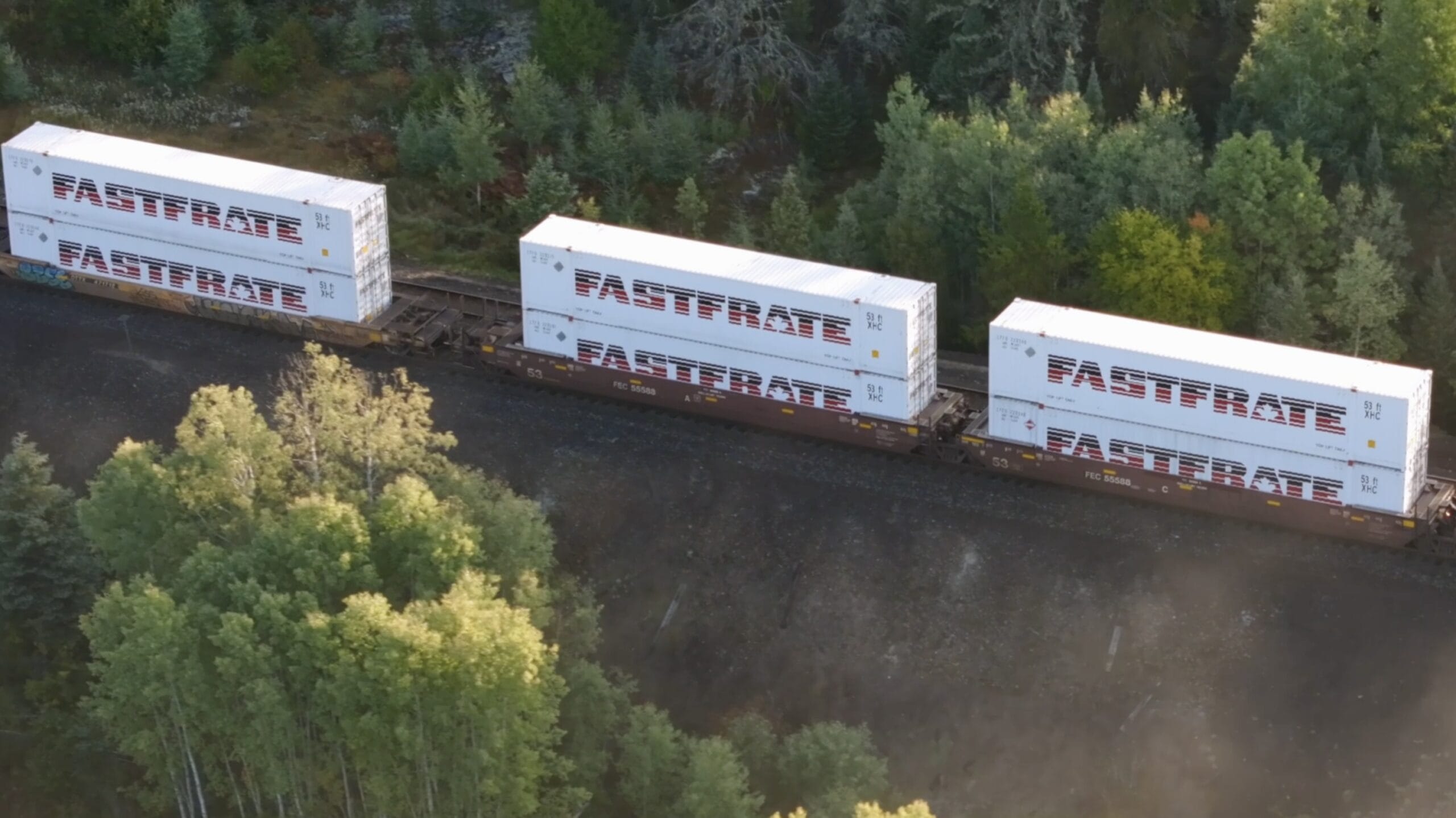 Three freight containers labeled "FASTRATE" on a train track surrounded by trees