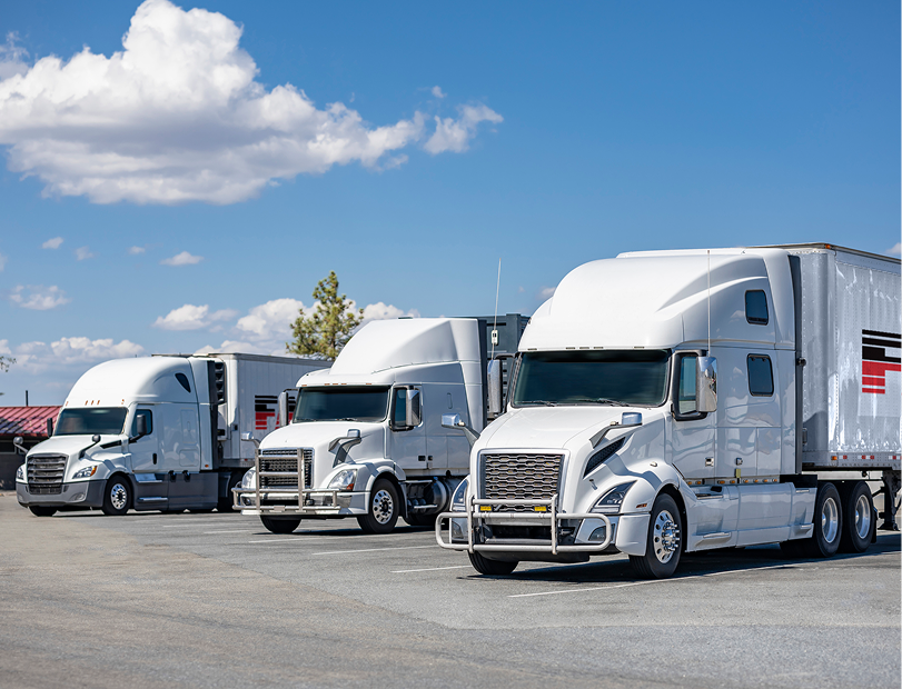Three white semi-trucks parked under a blue sky with clouds