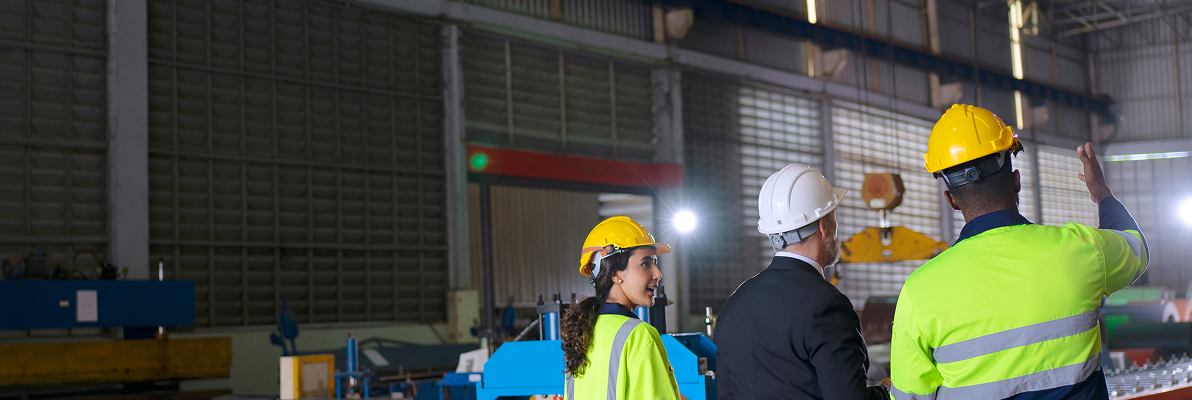 Three workers in safety gear discussing in a warehouse setting
