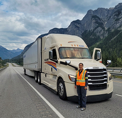 Truck driver in safety vest standing beside a large truck on a highway