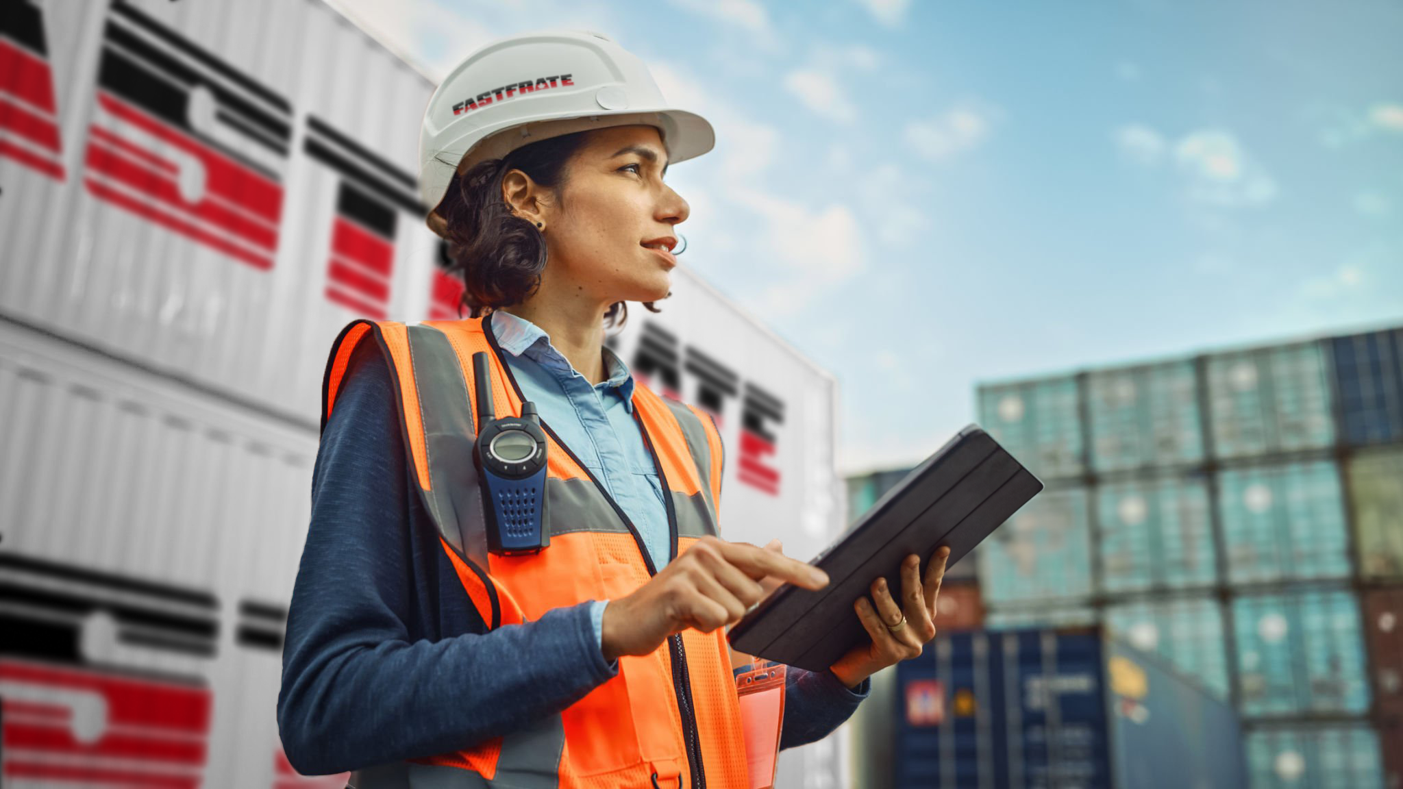 Woman in safety gear using a tablet near shipping containers