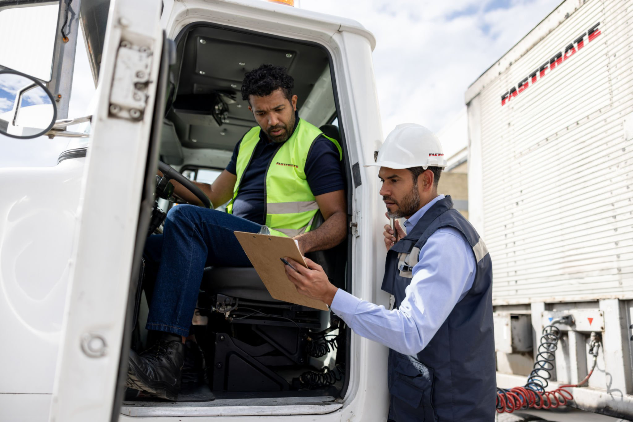 Two men discussing logistics near a truck, one seated inside and the other outside.