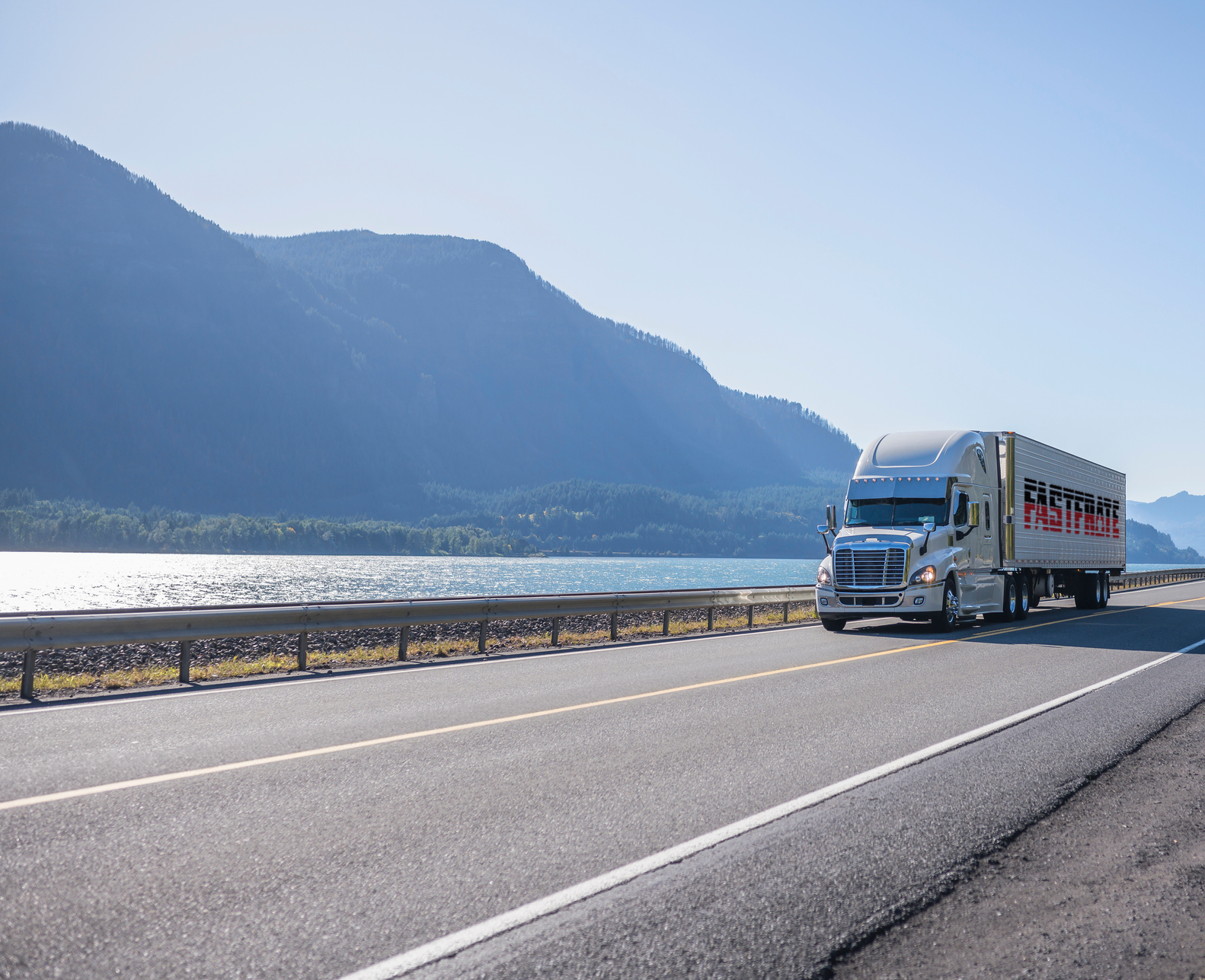 Truck driving along a scenic highway beside a lake and mountains