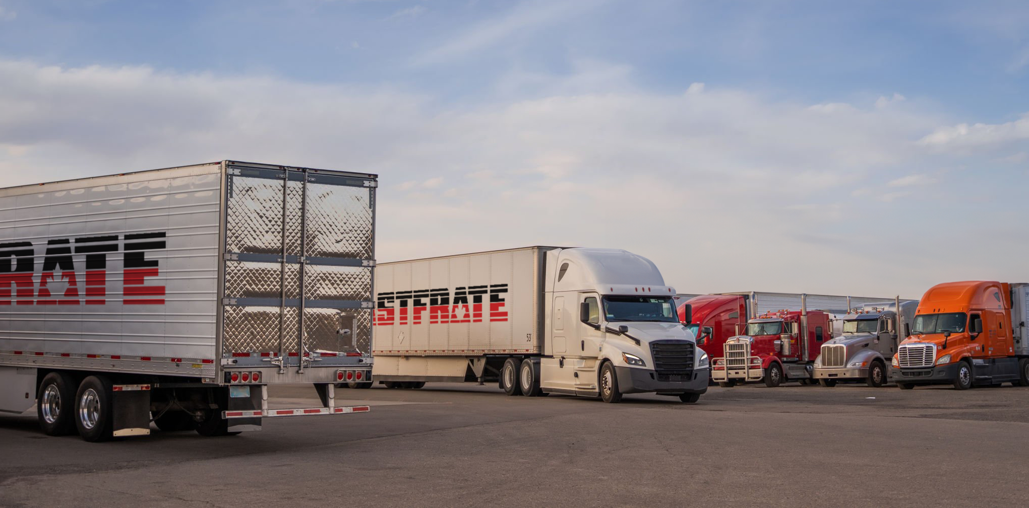 Trucks parked in a lot under a blue sky with clouds