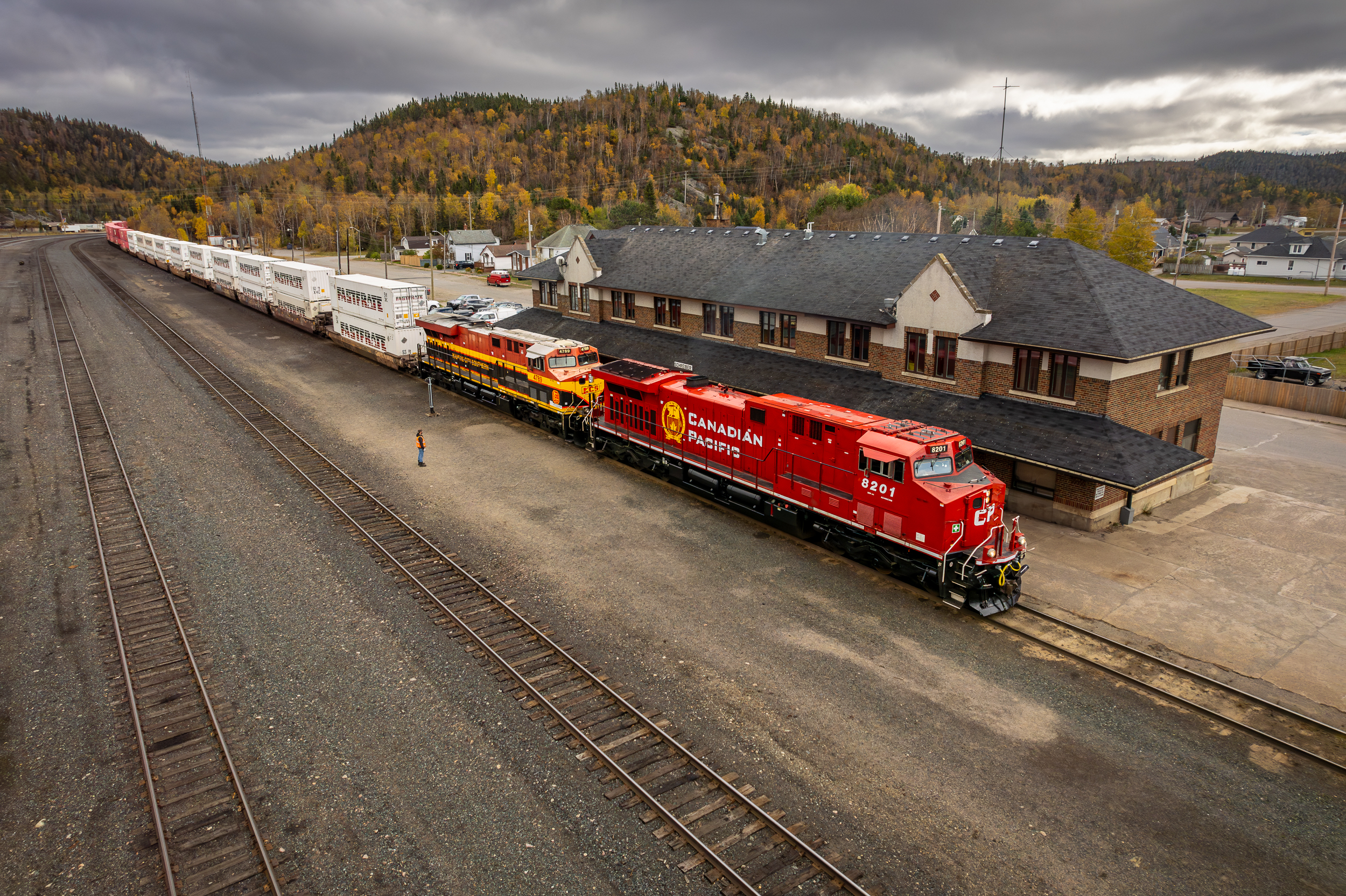 Red and yellow locomotives parked beside a train station in autumn scenery