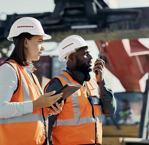Two construction workers in safety vests and helmets communicate on a site