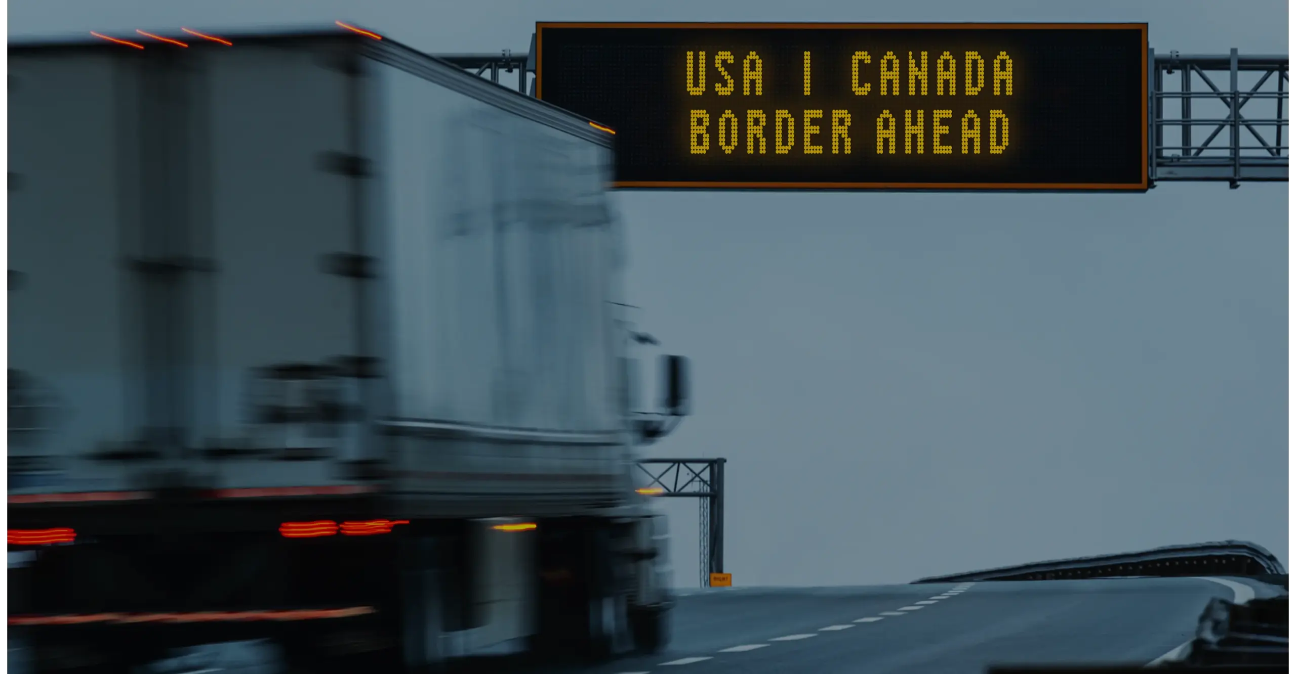 Truck driving on highway with border sign reading "USA | CANADA BORDER AHEAD