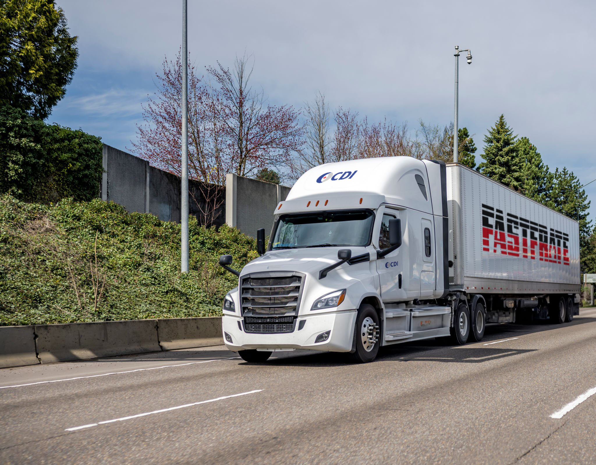 White semi-truck driving on a highway with green trees in the background