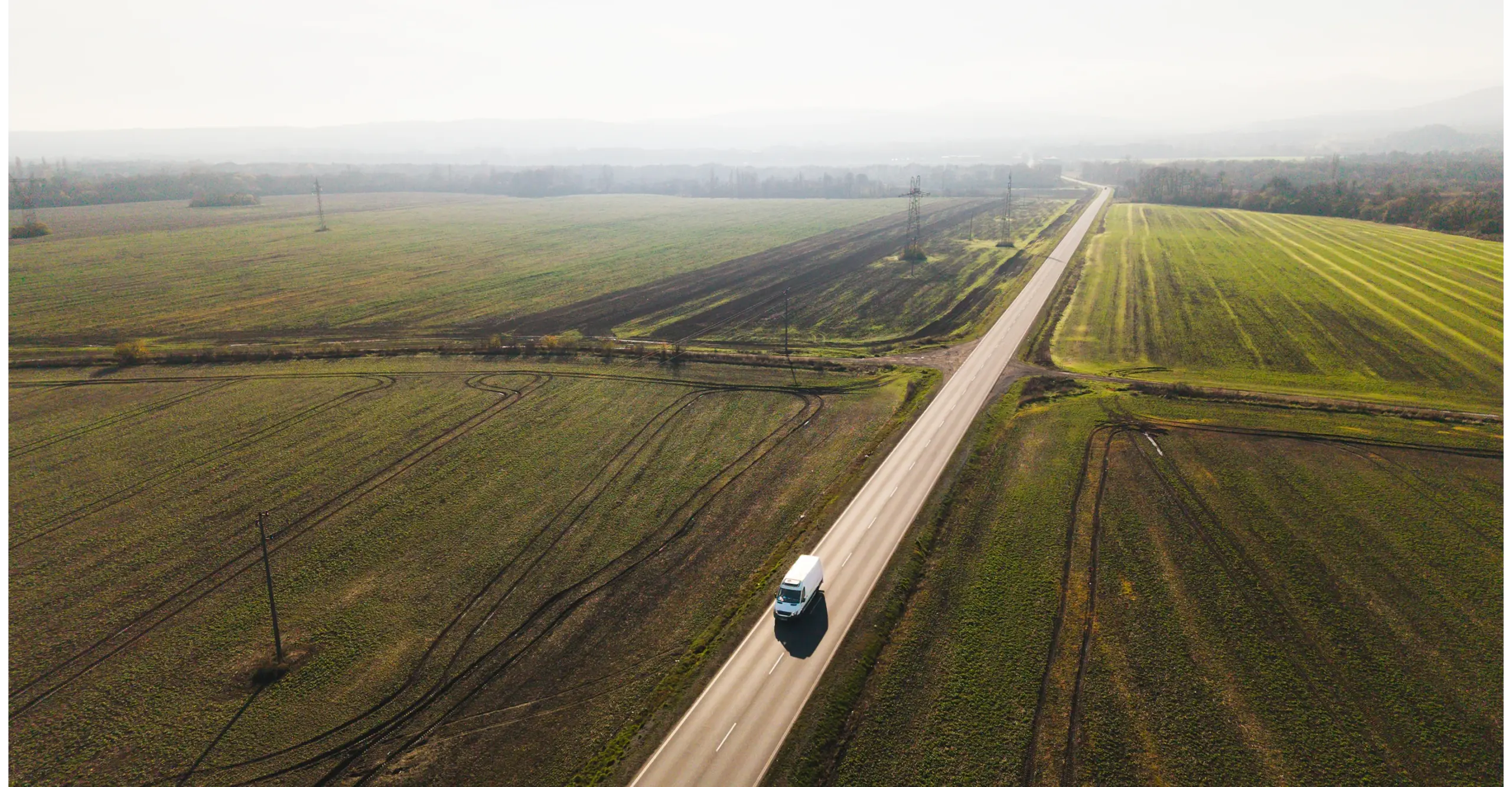 Aerial view of a van driving on a rural road through green fields