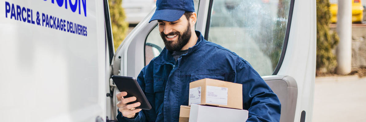 Delivery driver holding packages and checking a device in a van doorway