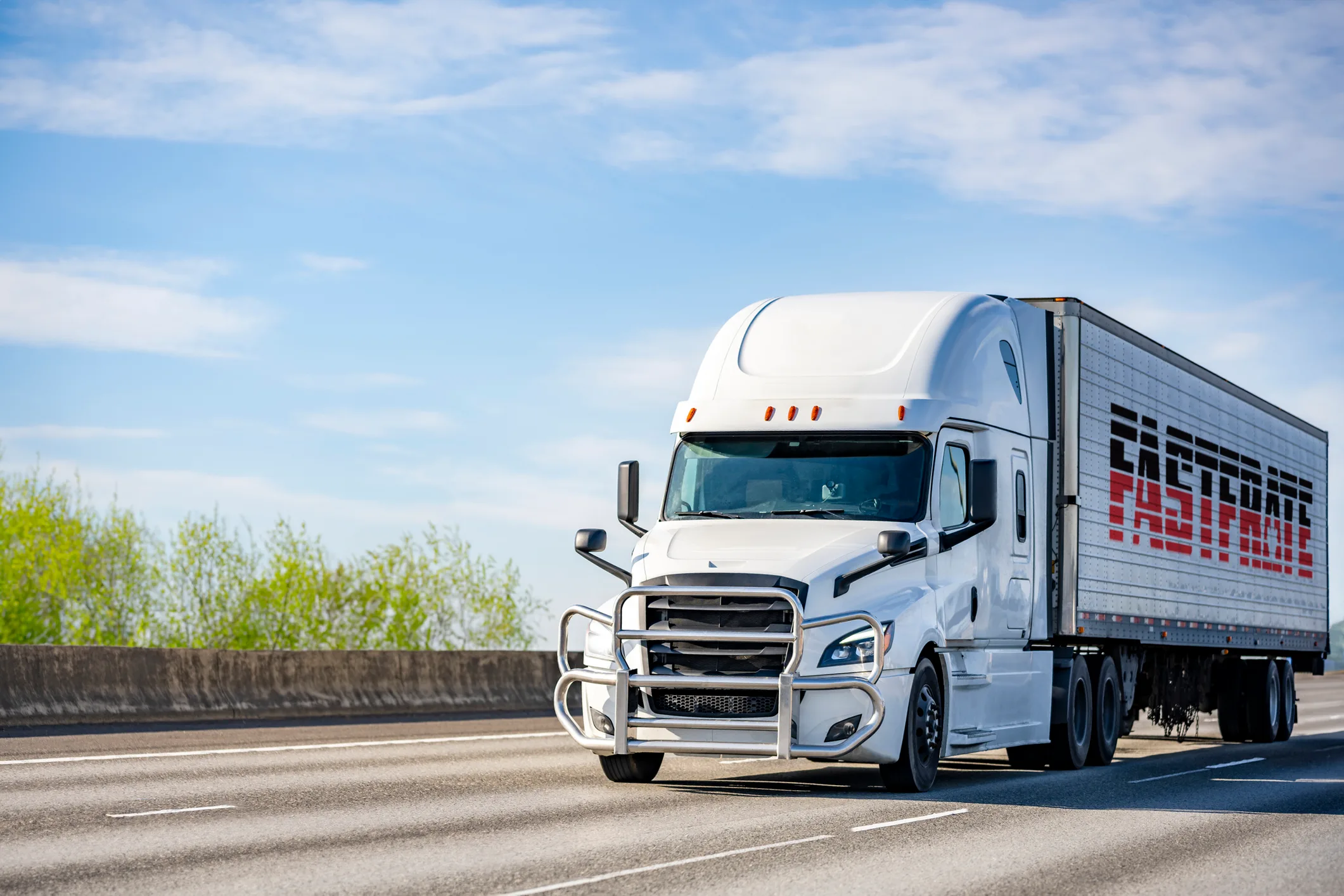 White semi-truck driving on a highway under a blue sky