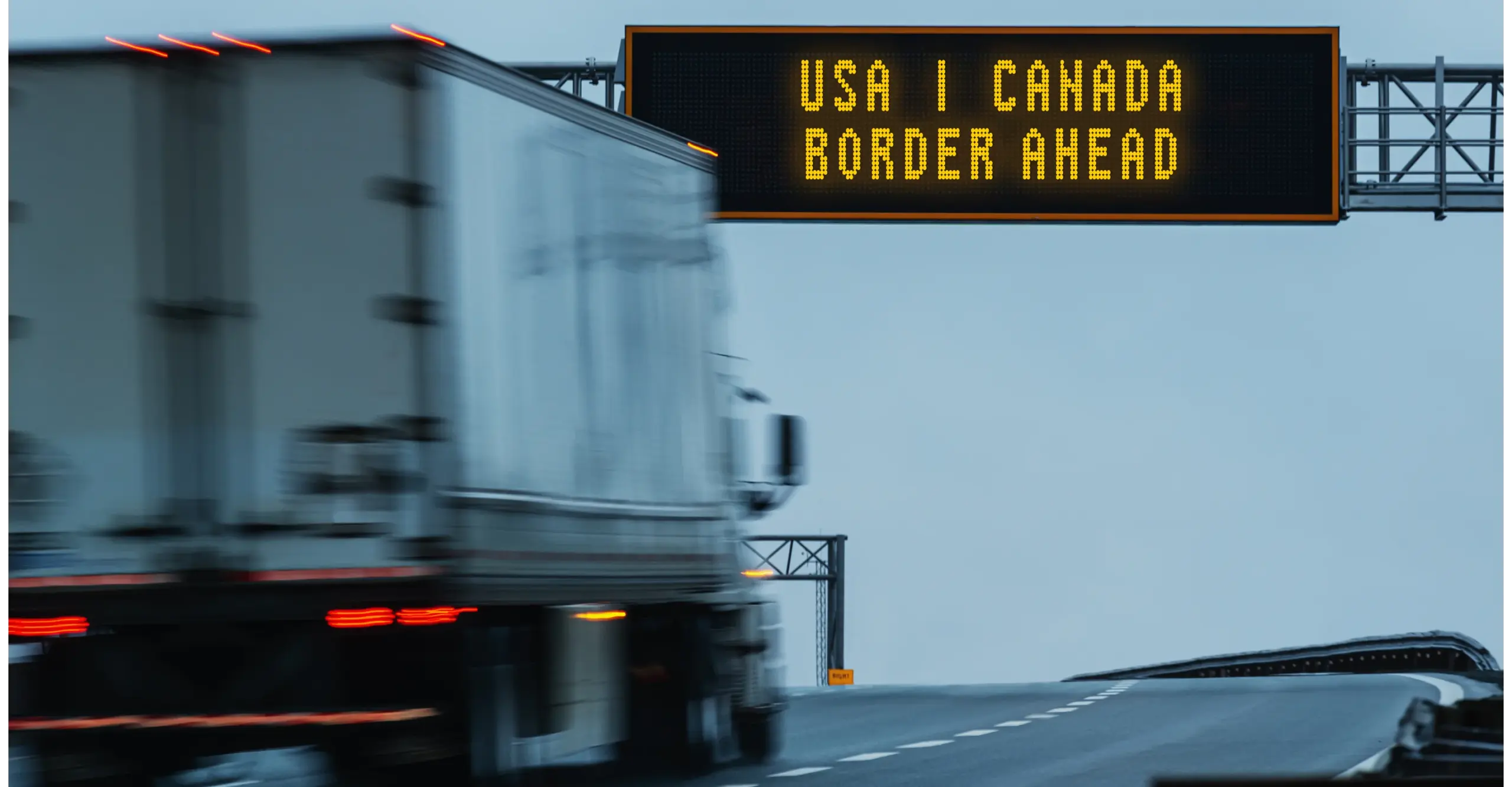 Truck driving on highway with border sign reading "USA | CANADA BORDER AHEAD