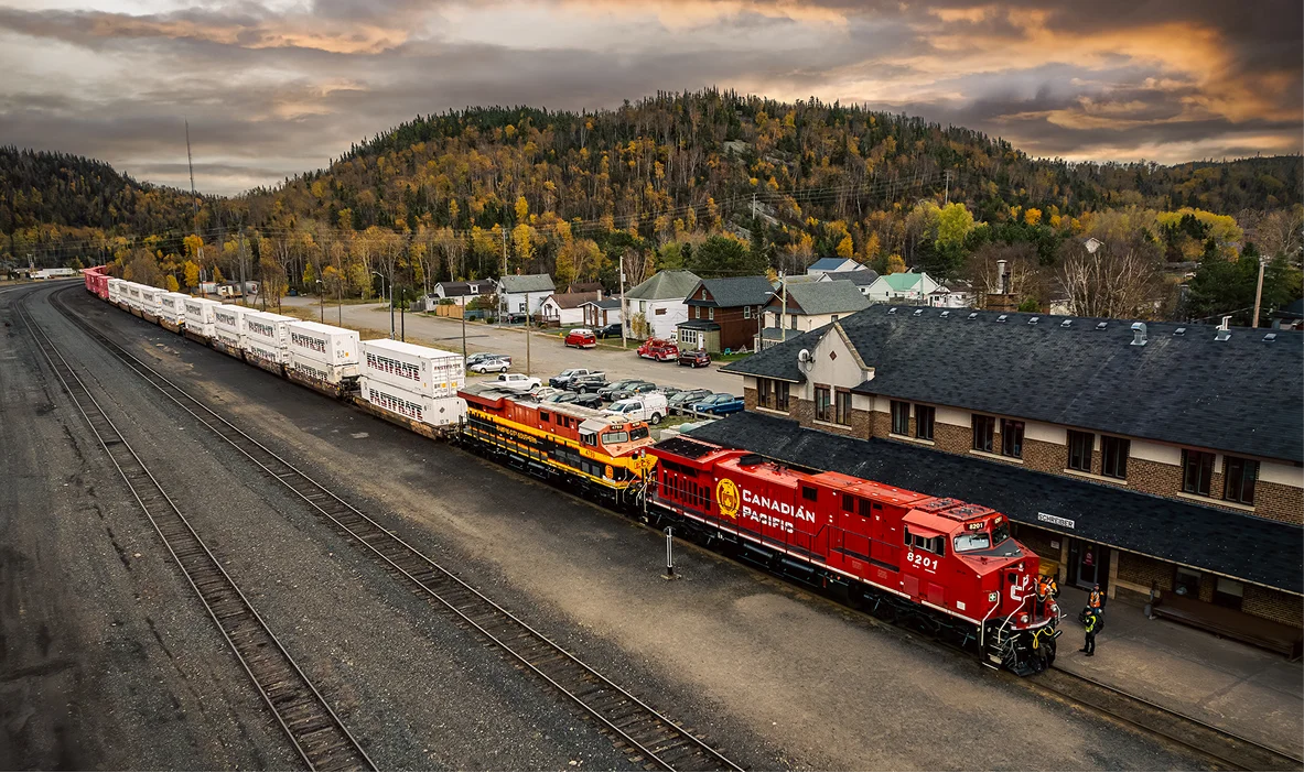 Red locomotive parked beside a train station with mountains in the background