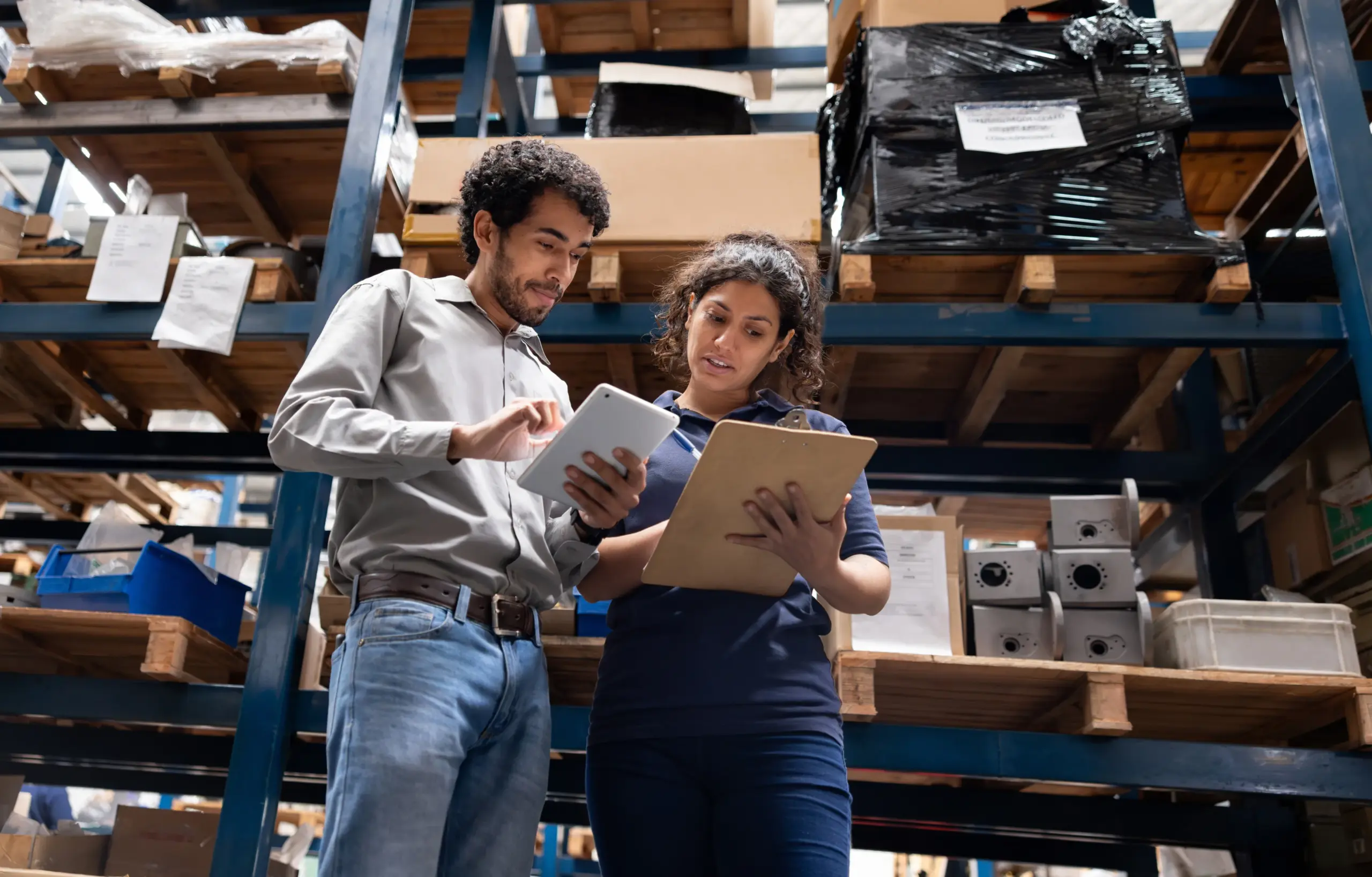 Two warehouse workers discussing inventory on a tablet and clipboard