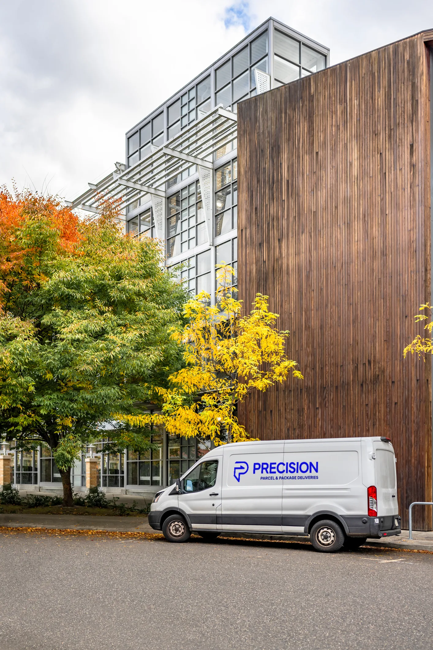 Delivery van parked near a modern building with autumn trees