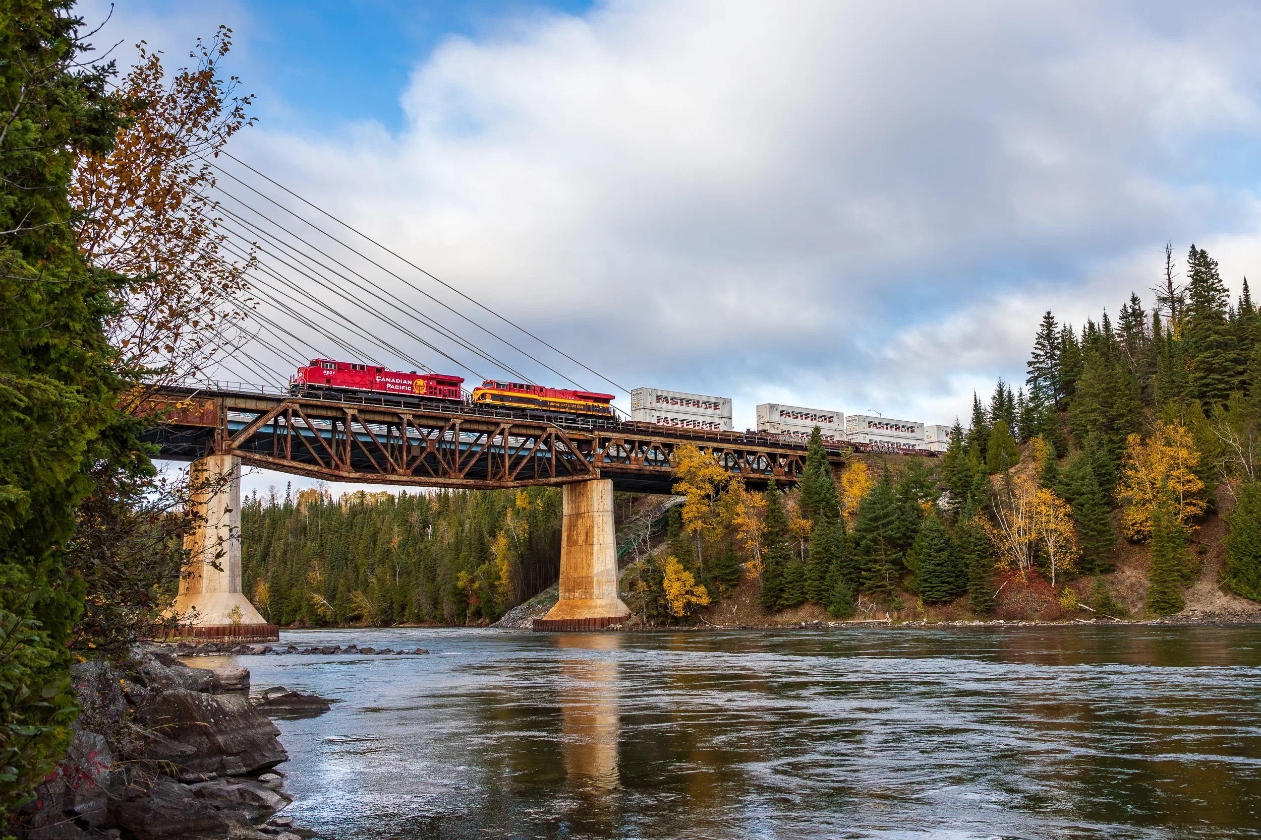 Train crossing a bridge over a river surrounded by autumn trees