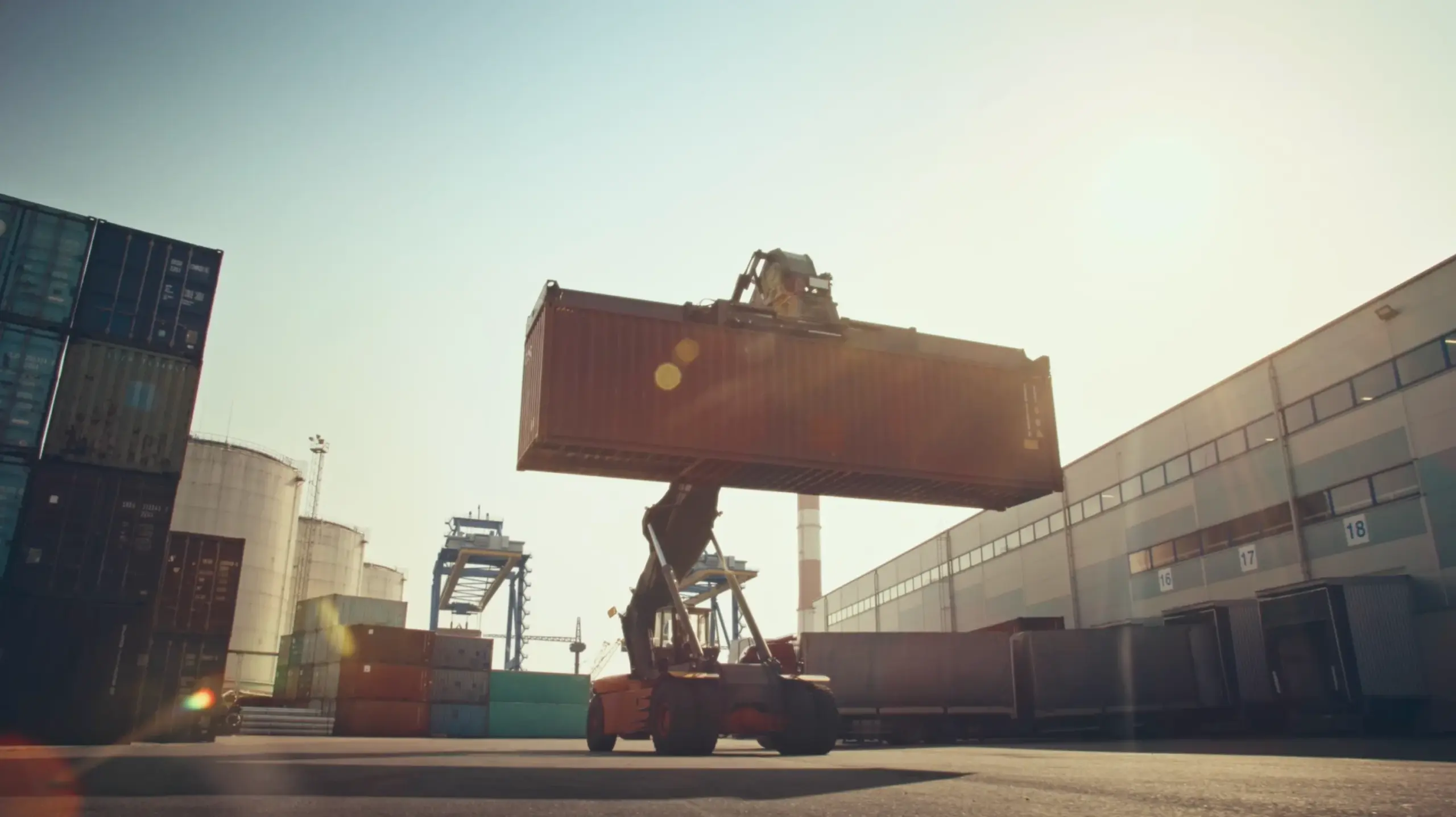 Forklift lifting a large shipping container at a port during sunset