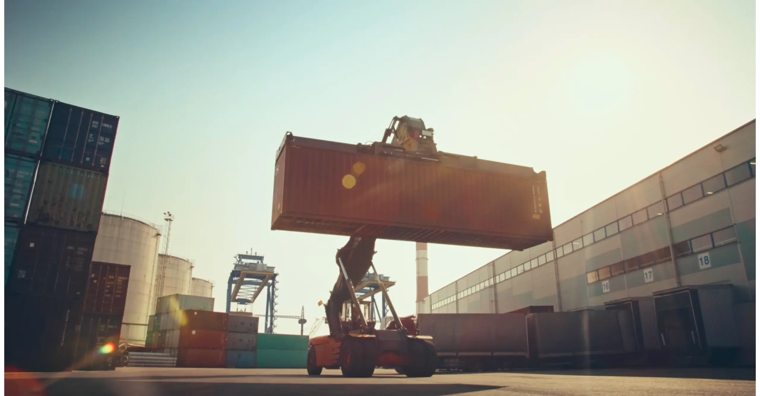 Forklift lifting a large shipping container at a port during sunset