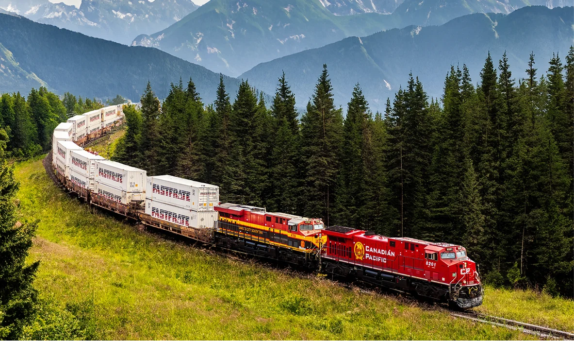 Freight train curving through lush green forest with mountains in background