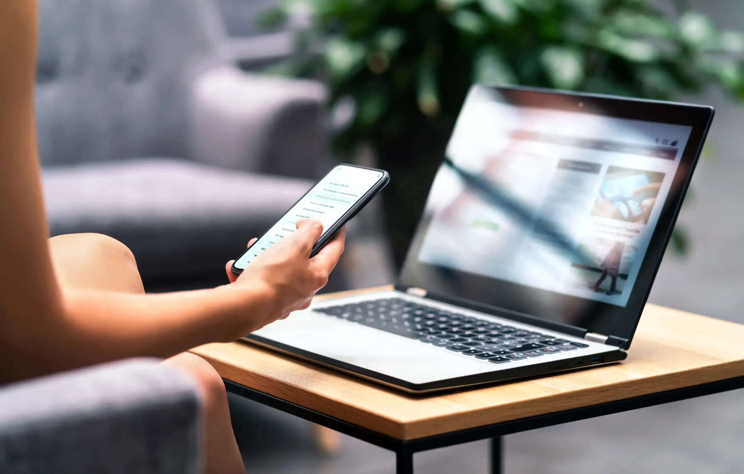 Person using a smartphone while sitting next to a laptop on a table