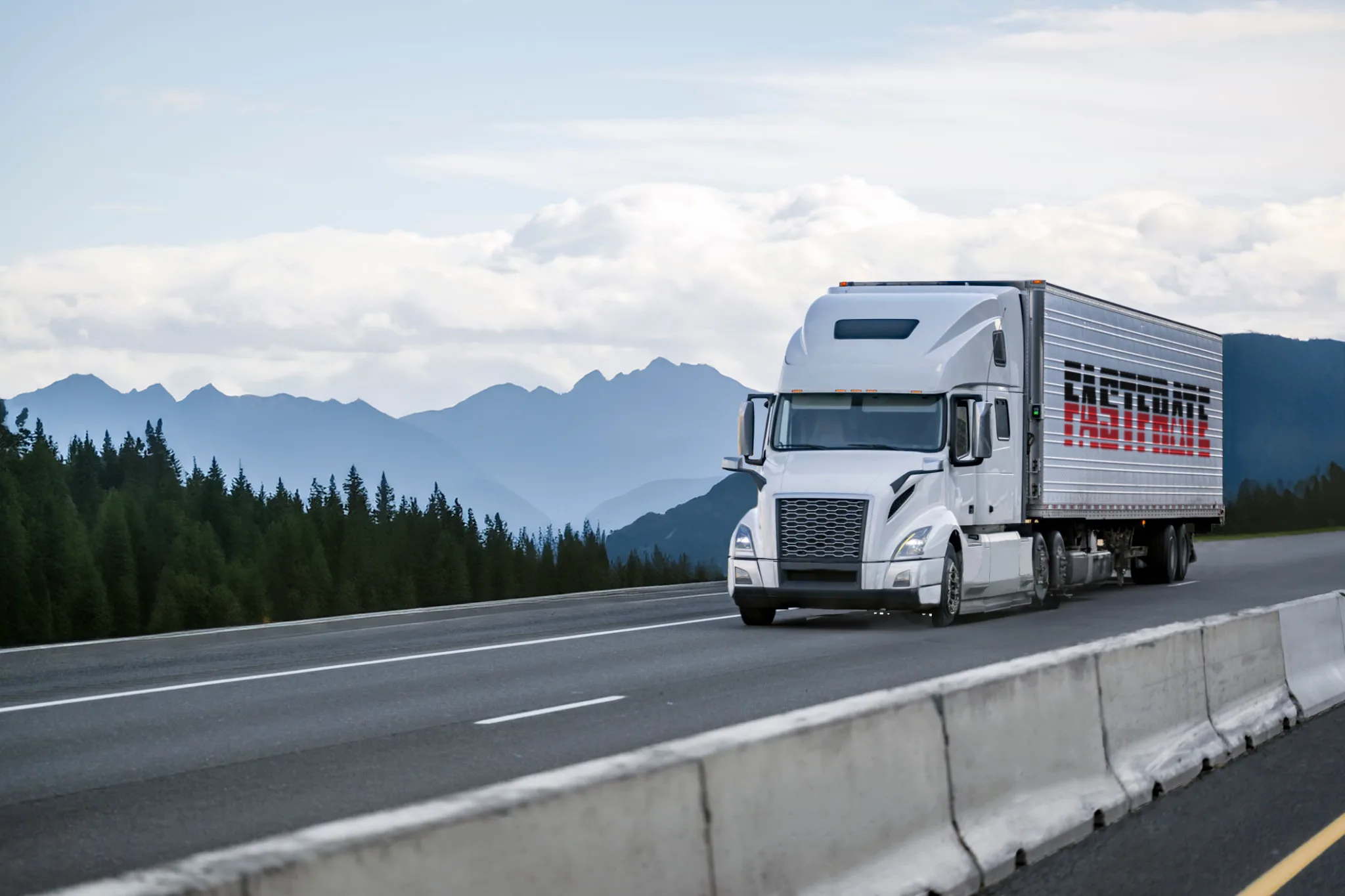 White freight truck driving on a highway with mountains in the background