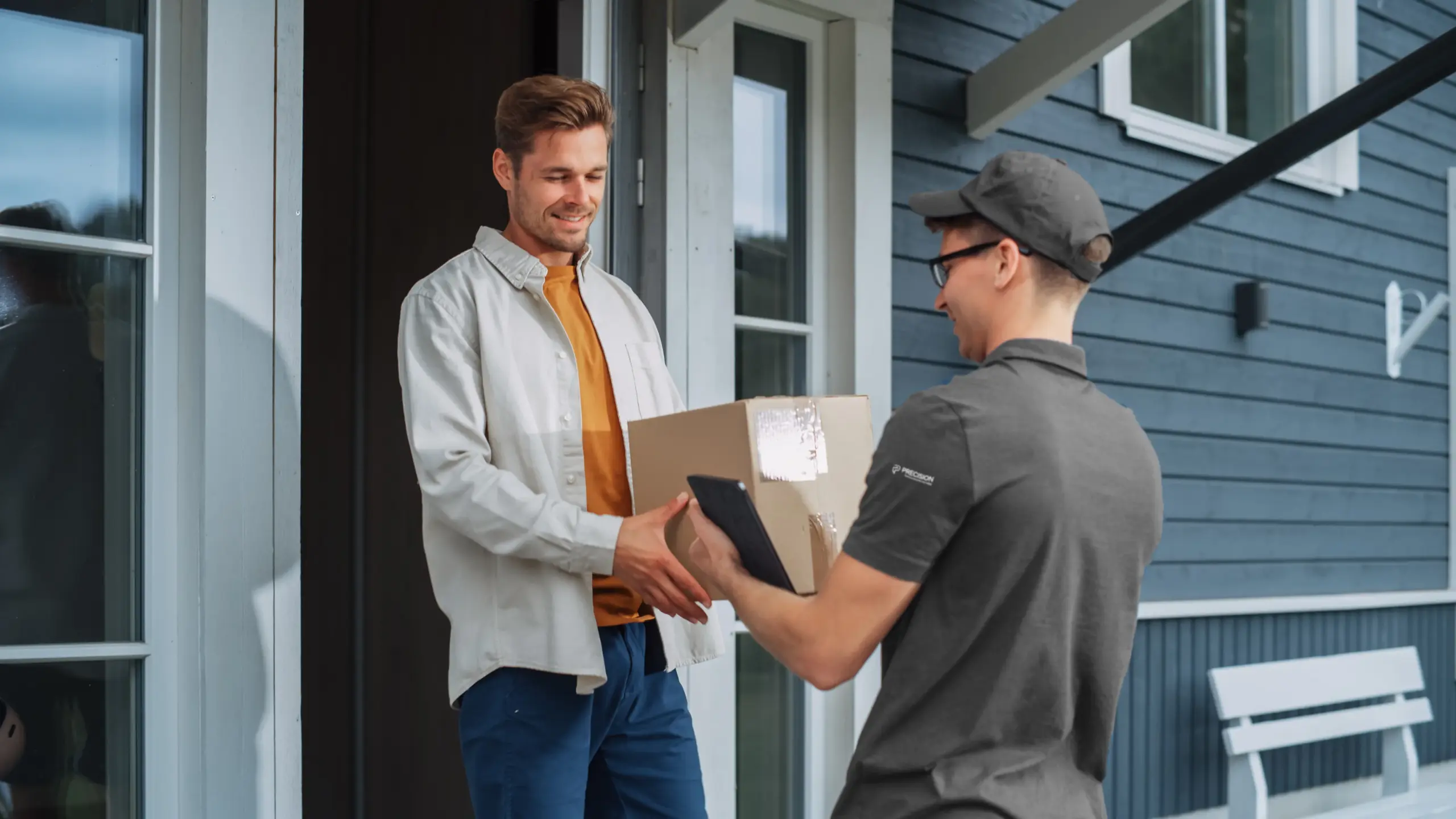 A delivery person hands a package to a smiling man at his doorstep