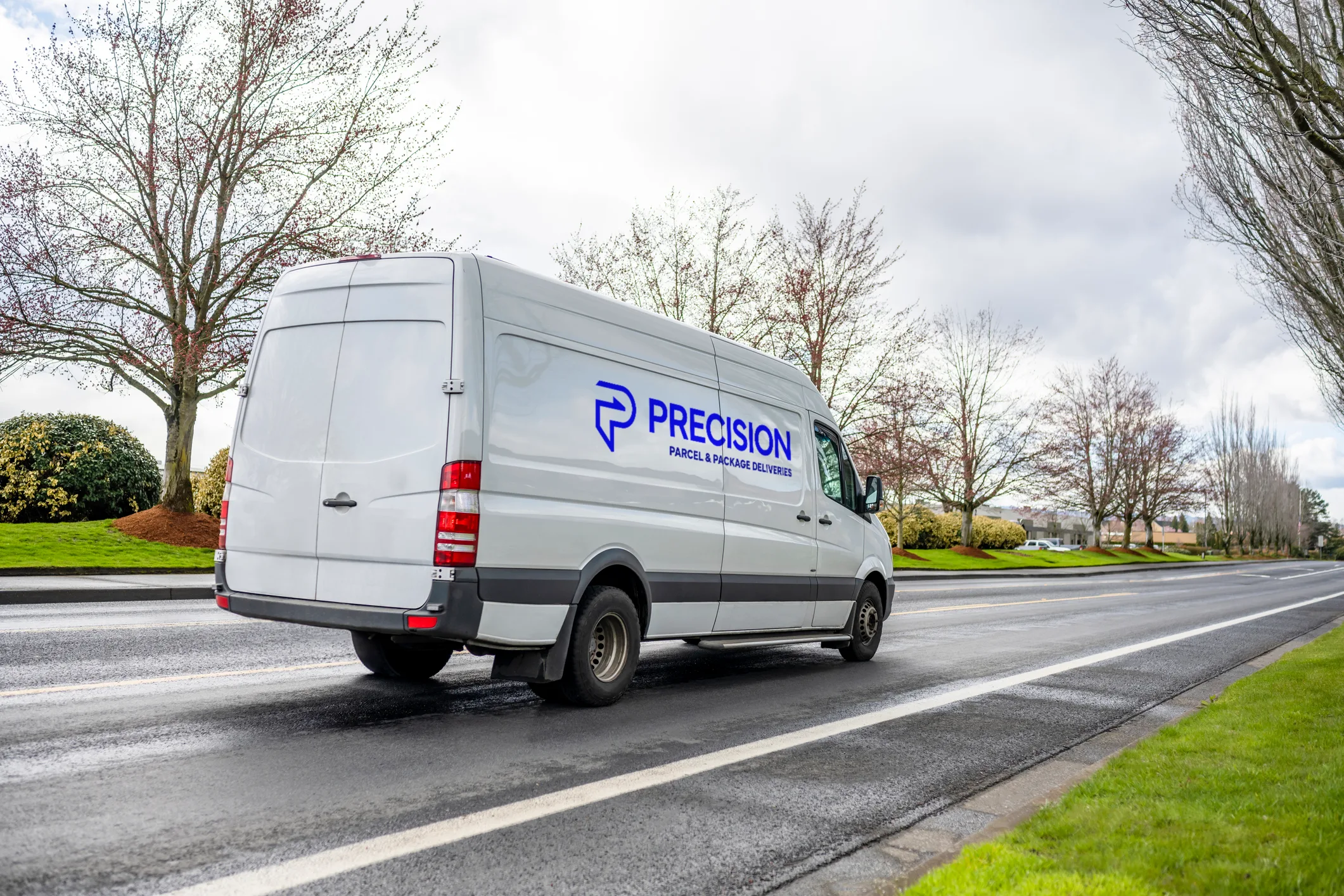 White delivery van with "Precision" logo driving on a tree-lined road