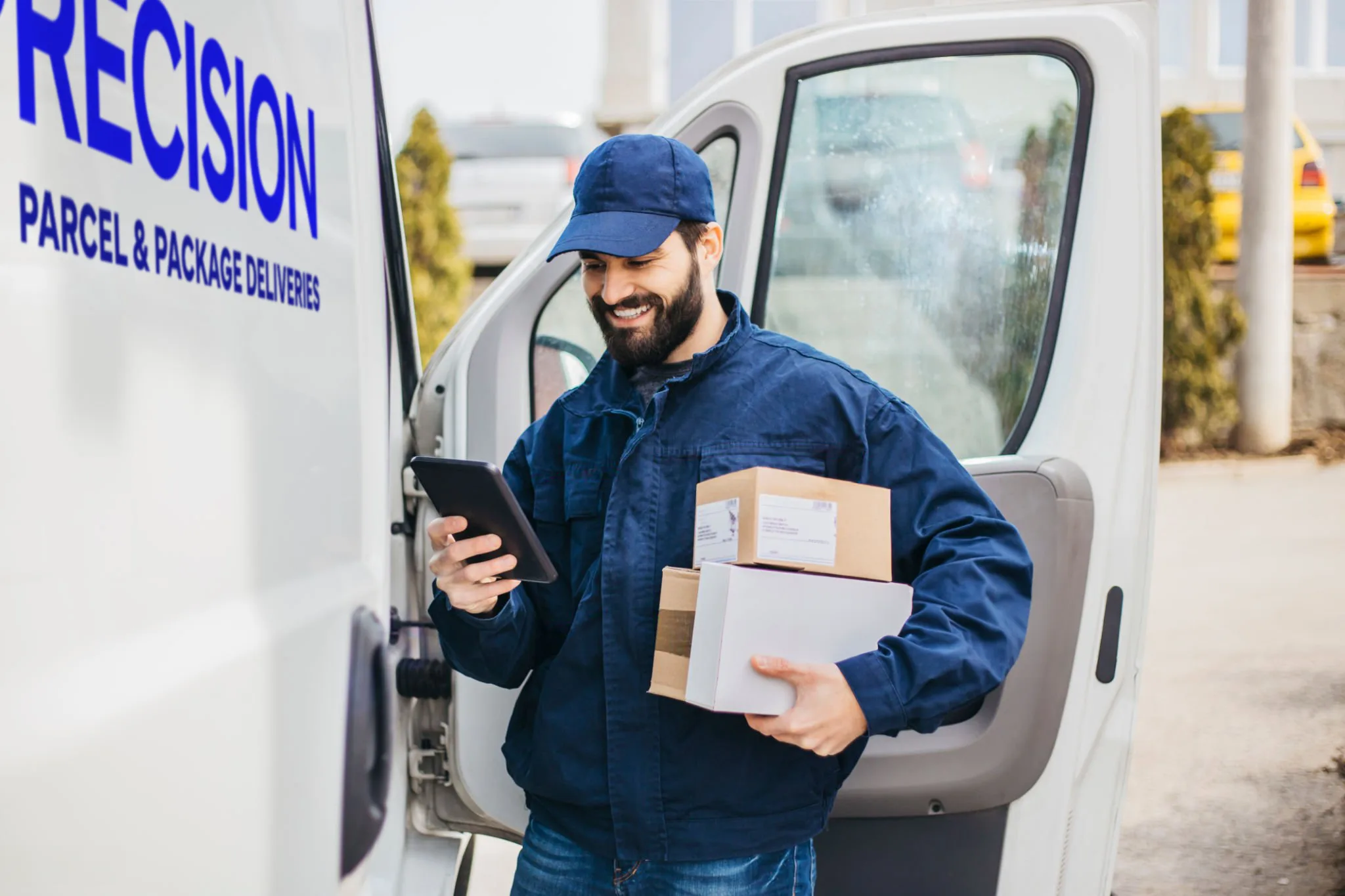 Delivery driver holding packages and checking phone by delivery van