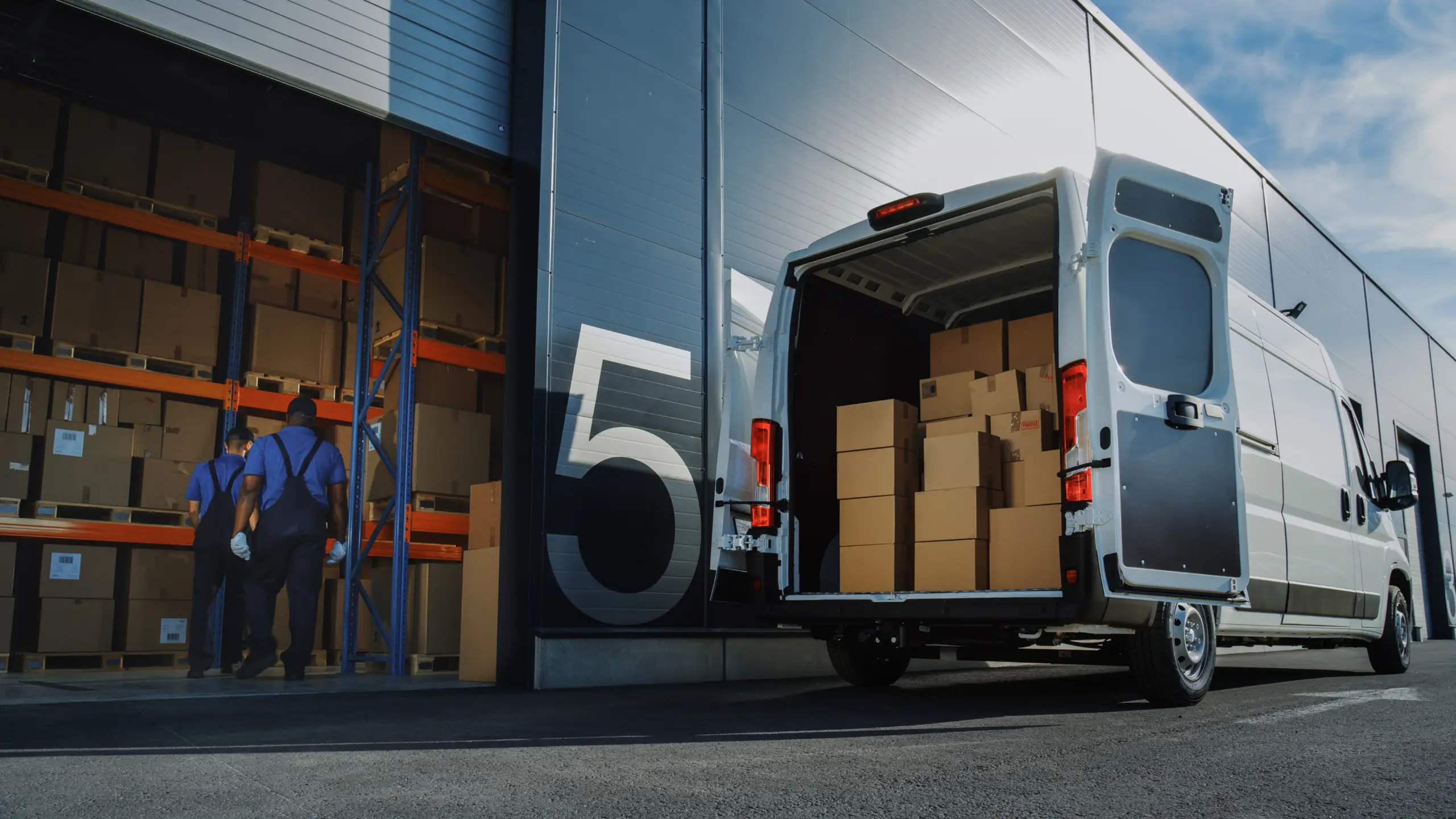 Delivery van parked at a warehouse with workers unloading boxes