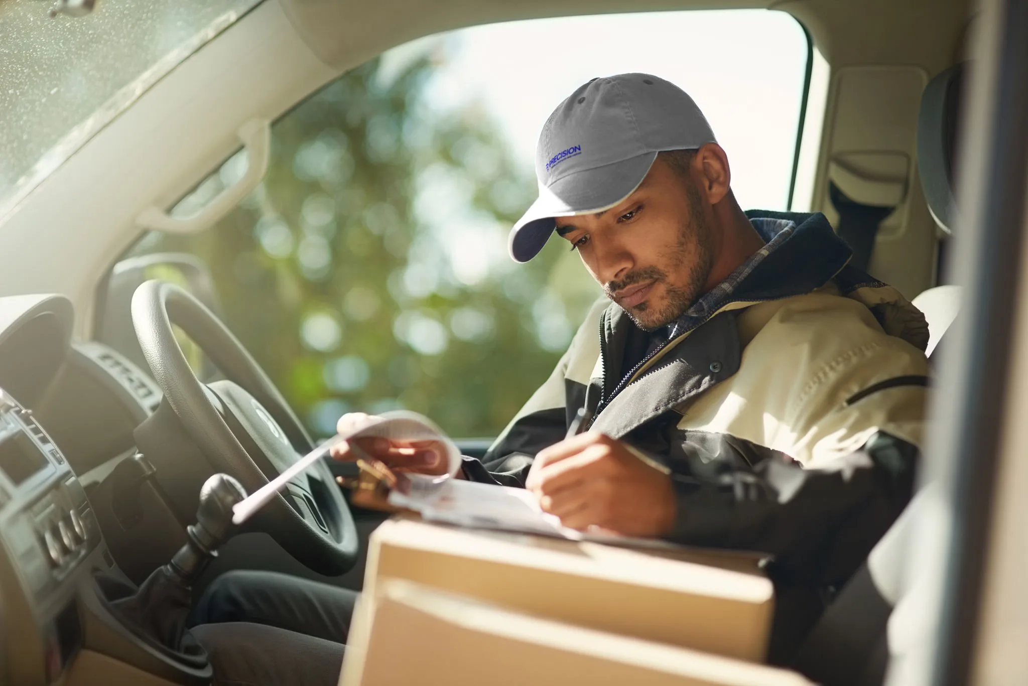 Delivery driver writing on a clipboard inside a vehicle with packages nearby
