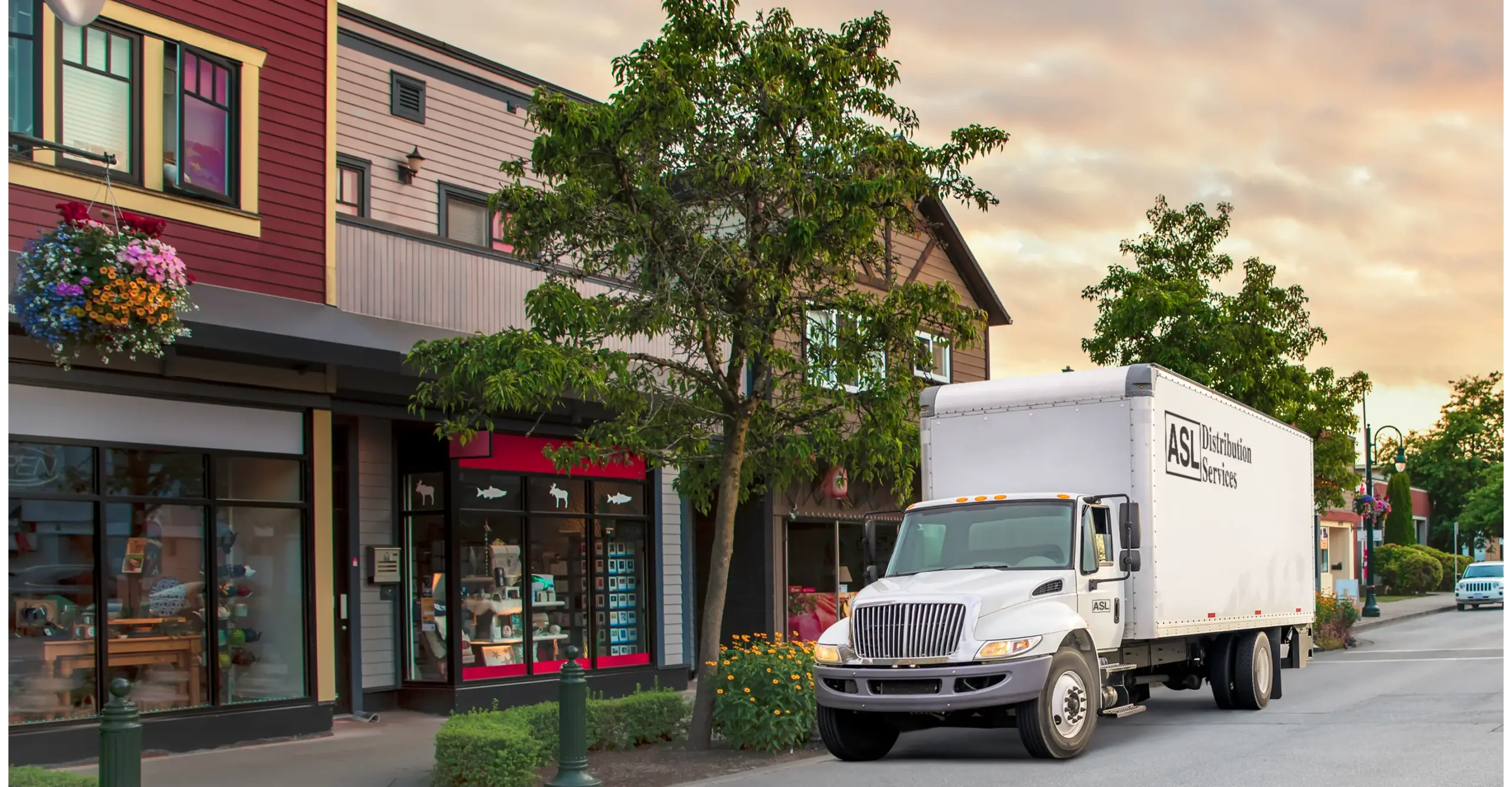 Delivery truck parked on a street near colorful storefronts and trees